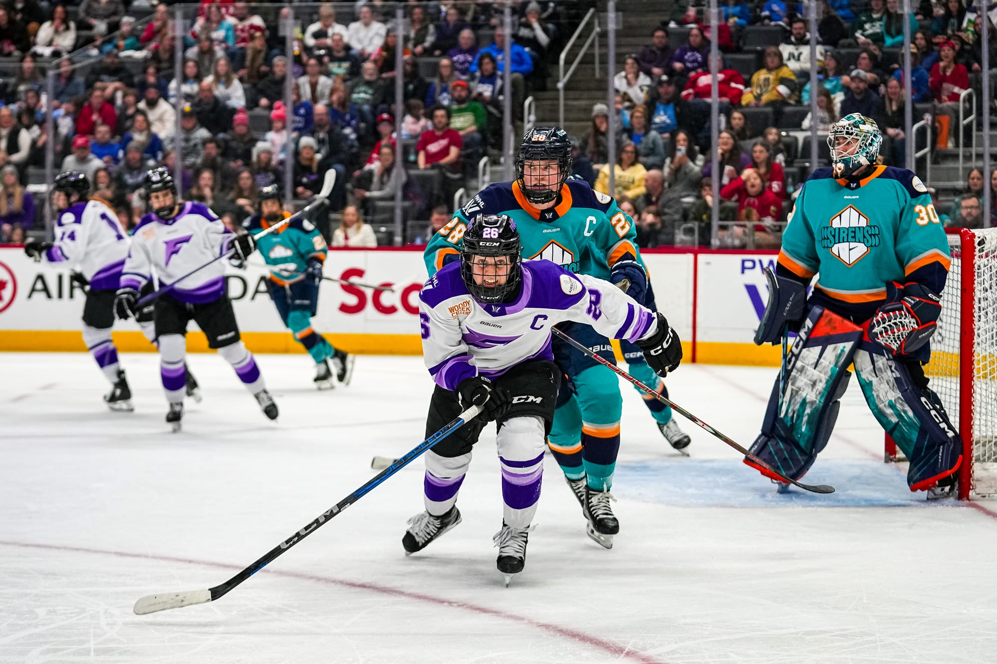 Coyne Schofield skates toward the camera, which is in the corner of the Frost's offensive zone. She is wearing a white away uniform.