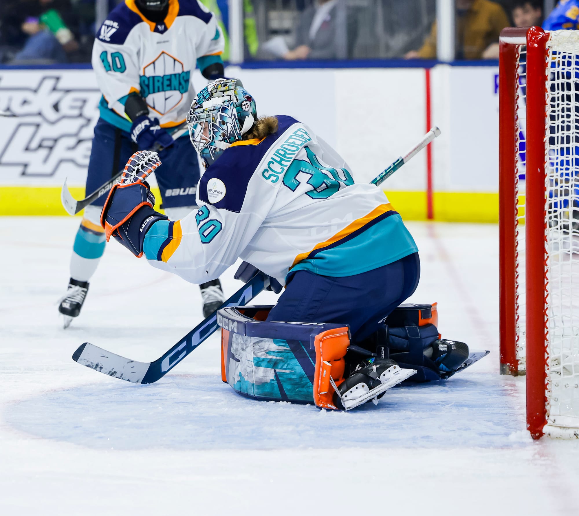 Schroeder is on her knees in the butterfly positioning, with her globe raised in front of her as she closes it on the puck. She is wearing a white away uniform.