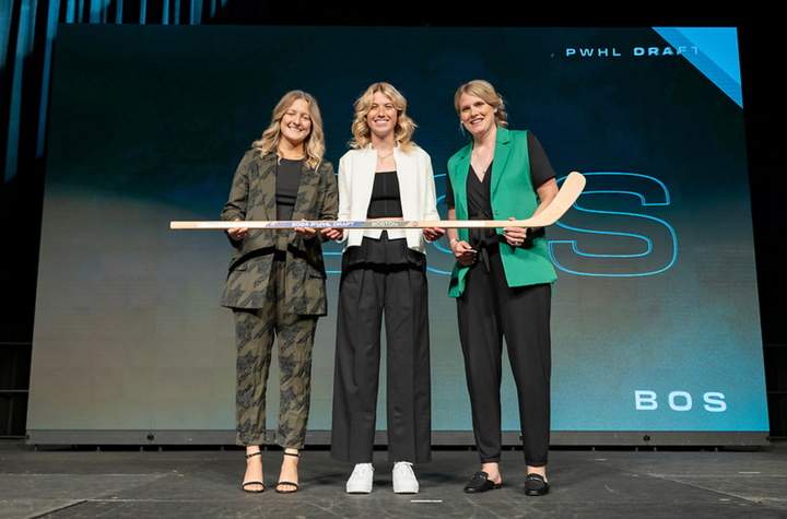 From left to right: Marmer, McMillan, and Kessel pose with a stick on stage, with a big screen behind them.