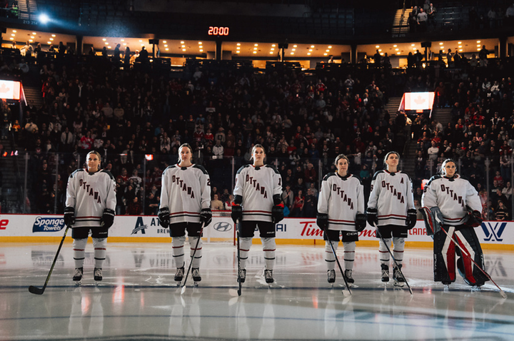 Six Ottawa players stand on the blue line before a game. They are all wearing white away uniforms.