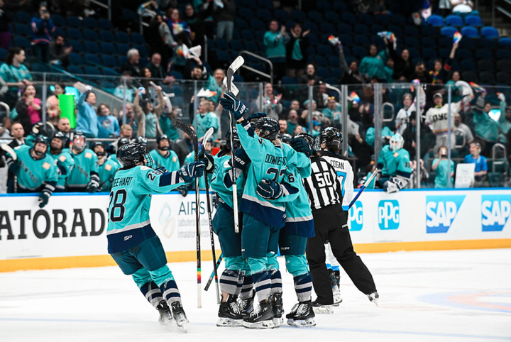 New York players celebrate a goal with a group hug. They are all wearing teal home jerseys.