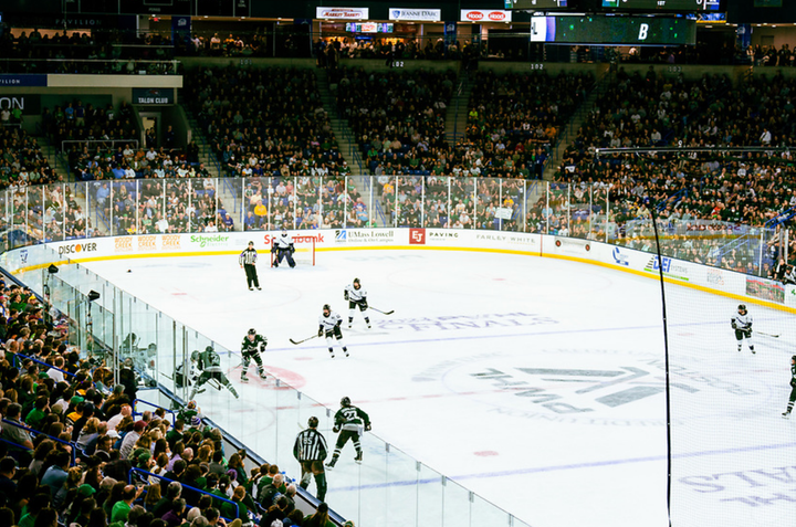 An above-ice level shot of Boston and Minnesota playing. There is an ongoing battle near the boards for the puck.