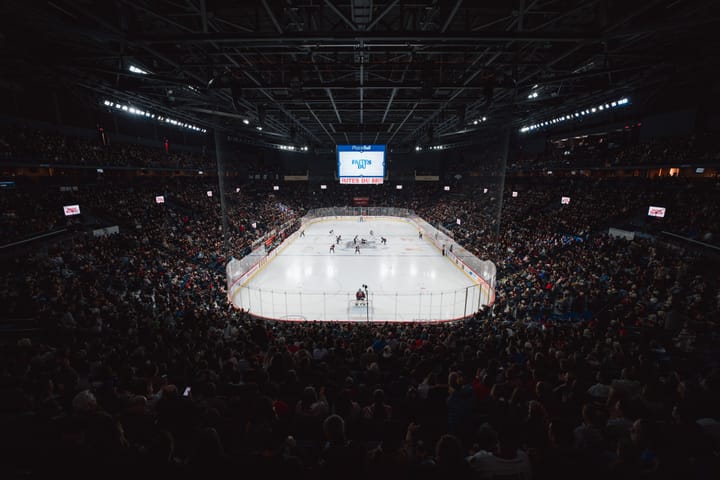 A wide-angle shot of the ice from behind Desbiens' net. The ice appears far away and the packed stands are also visible.