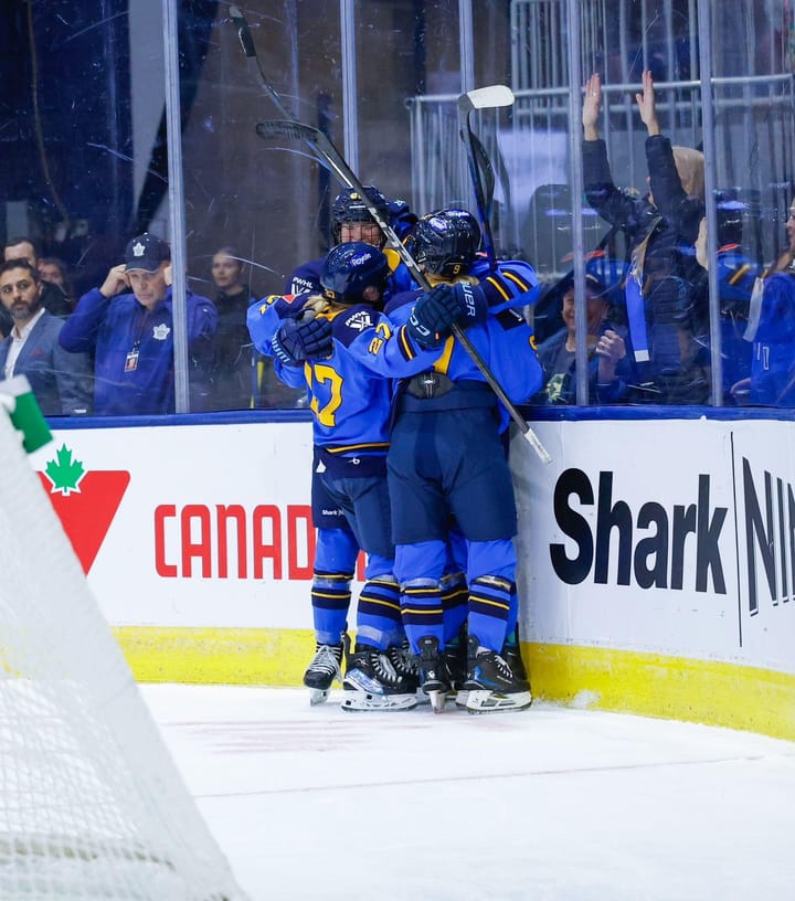 Sceptres players celebrate a goal with a tight group hug behind the net. They are wearing blue home uniforms.