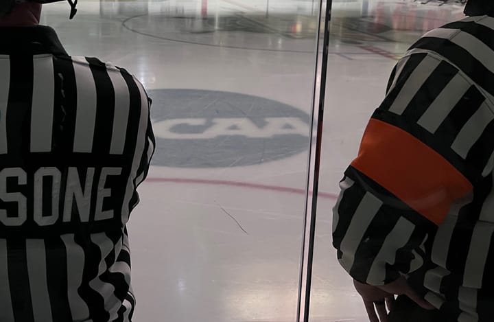 Two officials in black and white stripes with orange armbands are nearly ready for a game to start.