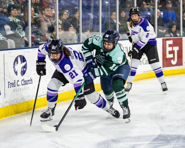 Bilka (right in green) and Schepers (left in white) battle for the puck along the boards.