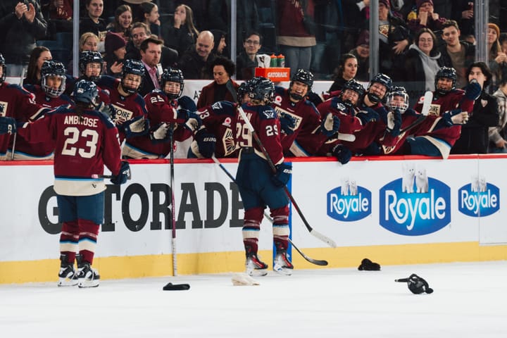 Poulin skates down the handshake line at the bench. Hats are scattered on the ice around her. She is wearing maroon.