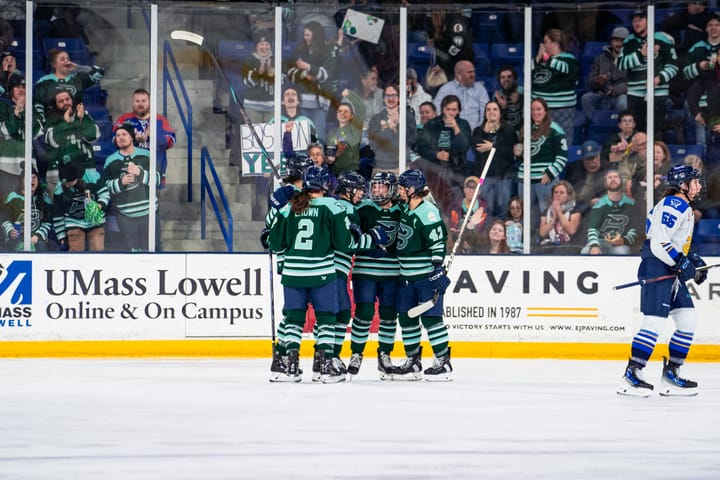 Five Fleet players celebrate a goal with a group hug. They are wearing green home uniforms.