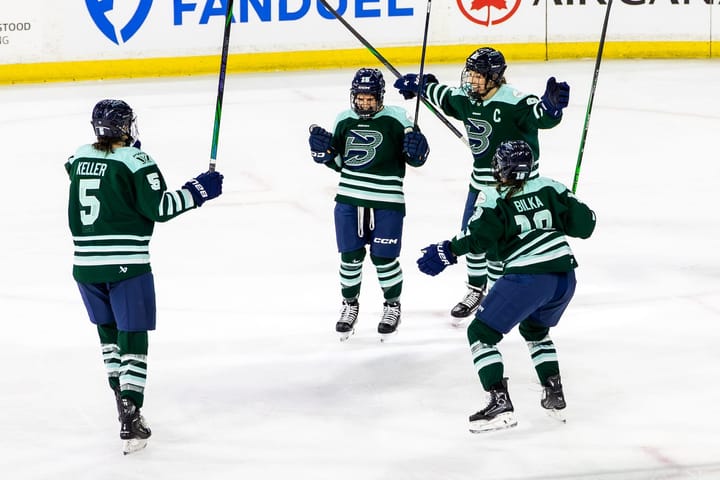 Four Fleet players celebrate a goal. They're skating toward each other for a group hug. They are wearing green home uniforms.