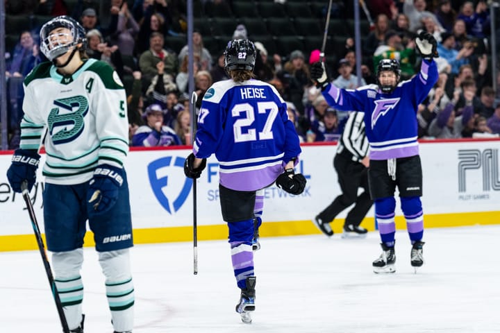 A from-behind picture of Heise lifting her leg and pumping her fists in celebration. She is wearing a purple uniform.