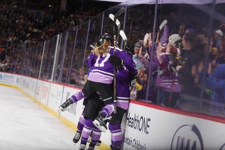 Minnesota players celebrate with a group hug. One is midair as they jump into the hug. They are wearing purple uniforms.