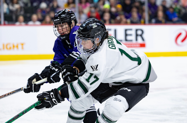 Girard (in white) reaches into a battle for the puck. The Minnesota player (in purple) is behind her to her right. 