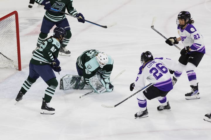 Peslarová crouches to freeze the puck against the Frost. She is wearing a green home uniform.