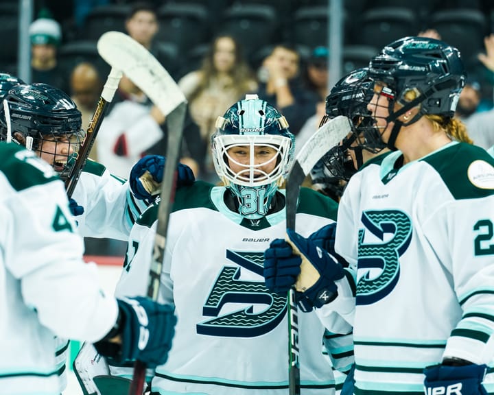 Frankel smiles as teammates come up and congratulate her. They are all wearing white away uniforms.