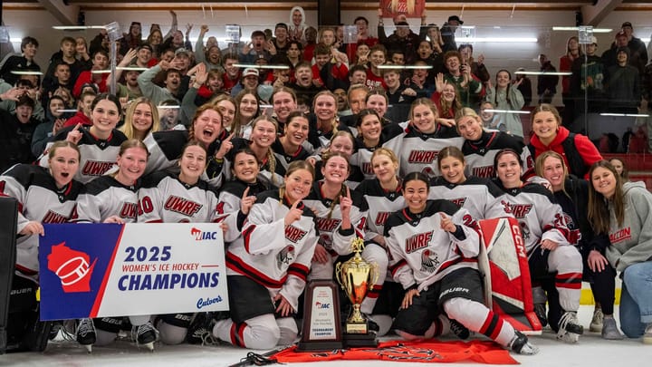 The UW-River Falls women's hockey team sits on the ice in front of the student section with their trophy and banner.