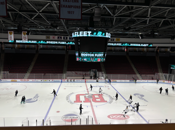 Several players are scattered around the BU ice in black and white jersey, as the jumbrotron shows Boston Fleet graphics